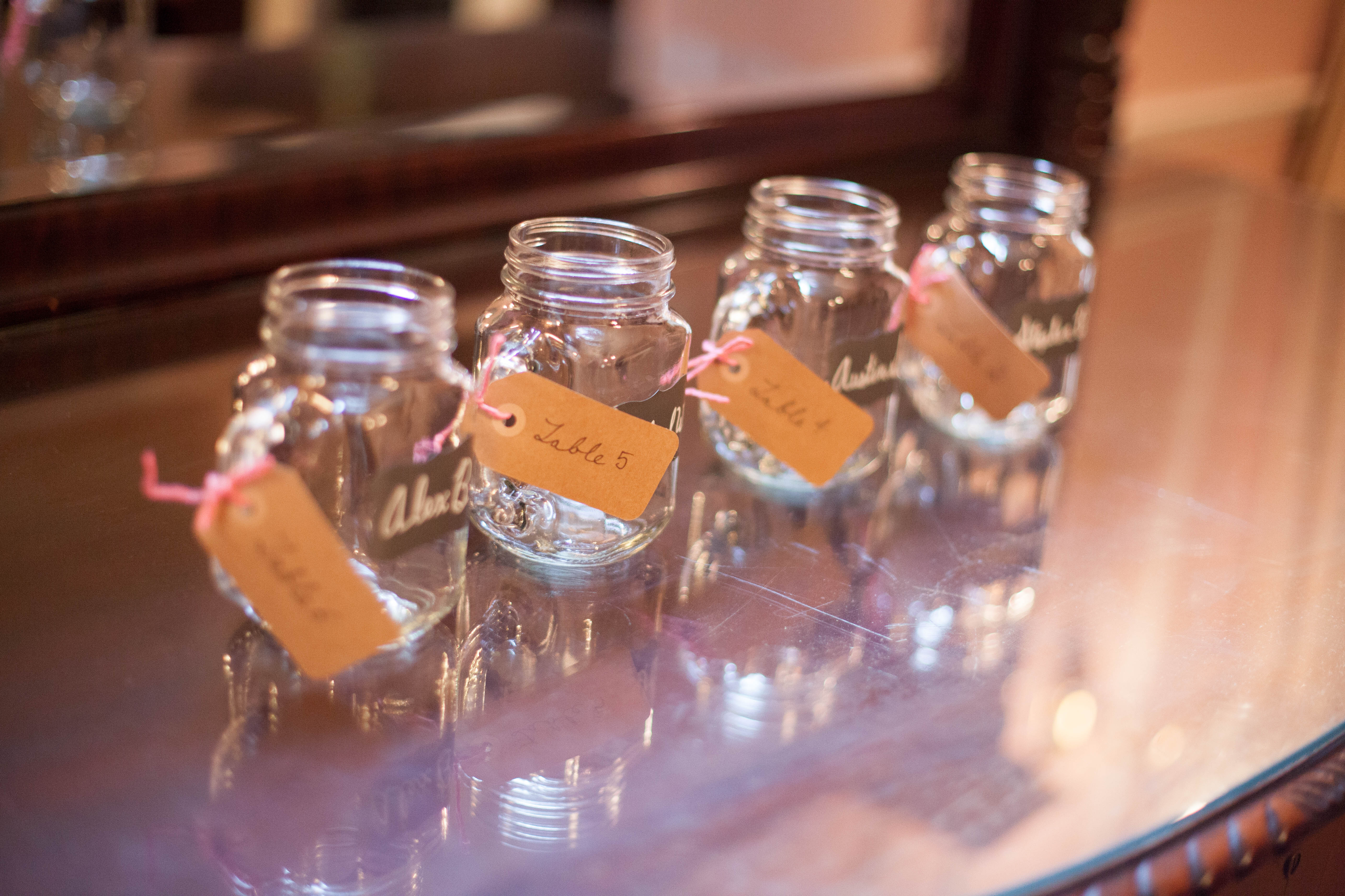 DIY Wedding project, escort cards with tables number tied to clear mason jars with handles with chalkboard label of guests name used as escort cards